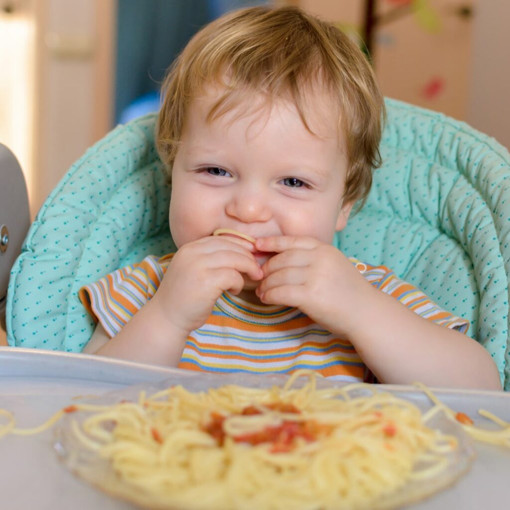 Niño pequeño comiendo con las manos, explorando la textura de los alimentos - beneficios del desarrollo sensorial en niños