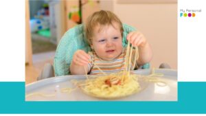 Niño pequeño comiendo con las manos, explorando la textura de los alimentos - beneficios del desarrollo sensorial en niños