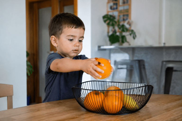 Niño pequeño colocando naranjas en el frutero de la cocina